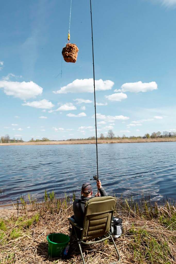 Рыбак сидя в кресле делает заброс фидером 