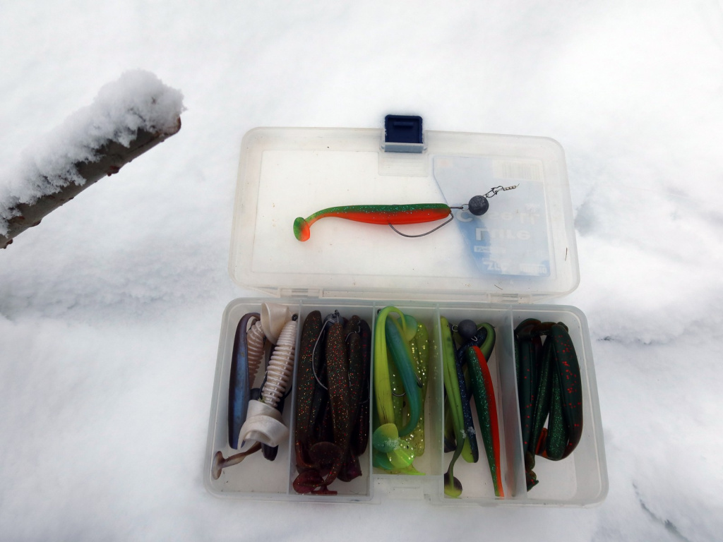 Открытая коробка с мягкими силиконовыми приманками лежит на снегу