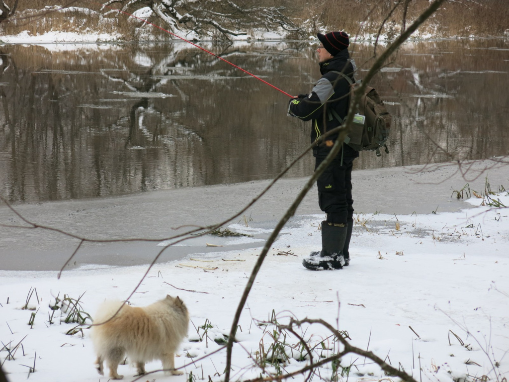 Рыбак ловит зимой спиннингом на берегу реки