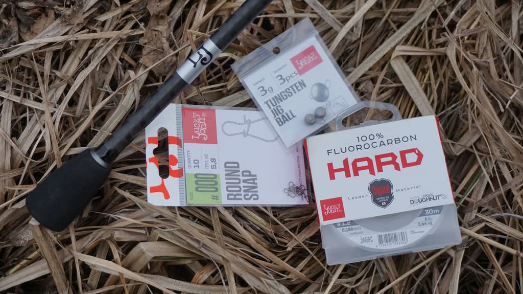 Спиннинг и оснастка Рукоять спиннинга и три упаковки с элементами оснастки лежат на сухой траве