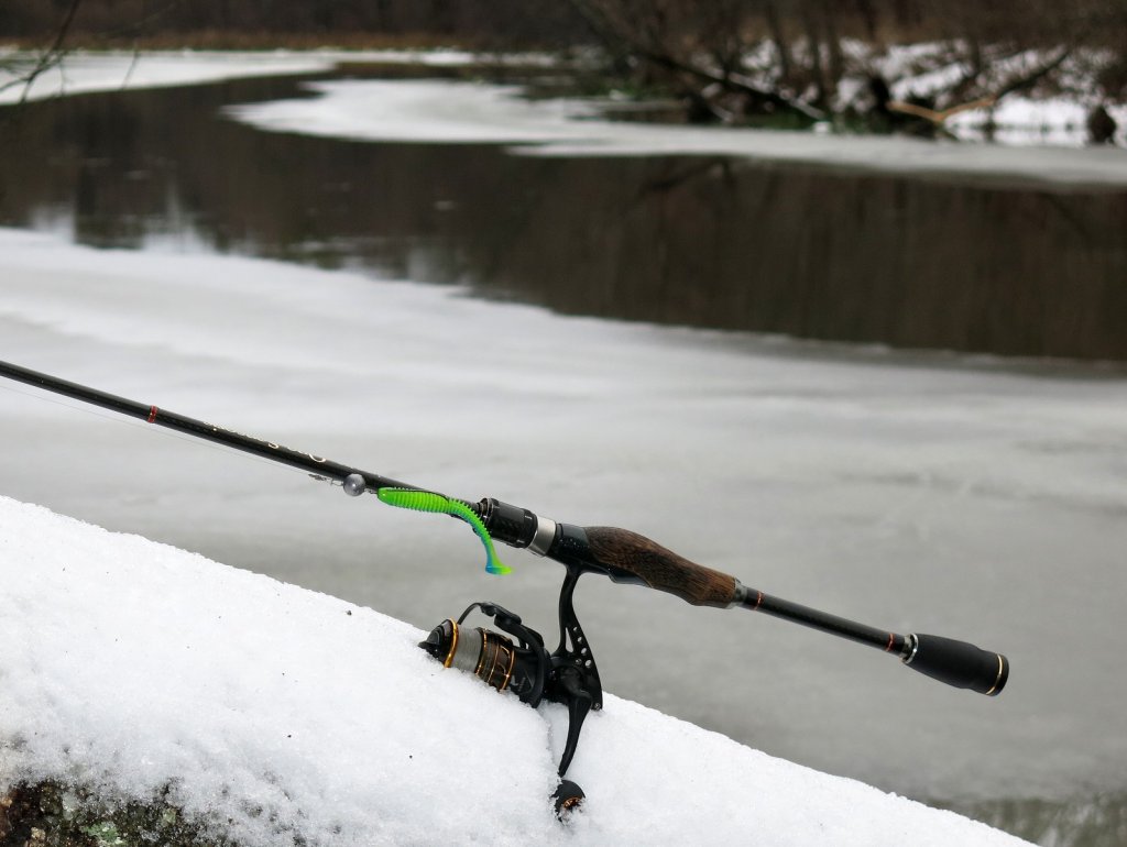 Спиннинг и мягкая приманка на фоне зимней реки