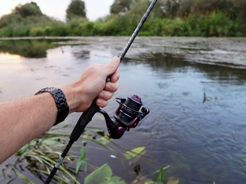 Спиннинговая снасть на фоне заросшей реки