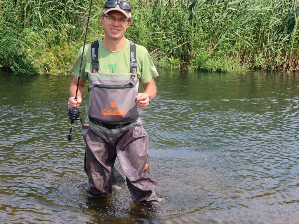 Довольный спиннингист идёт взабродку по реке