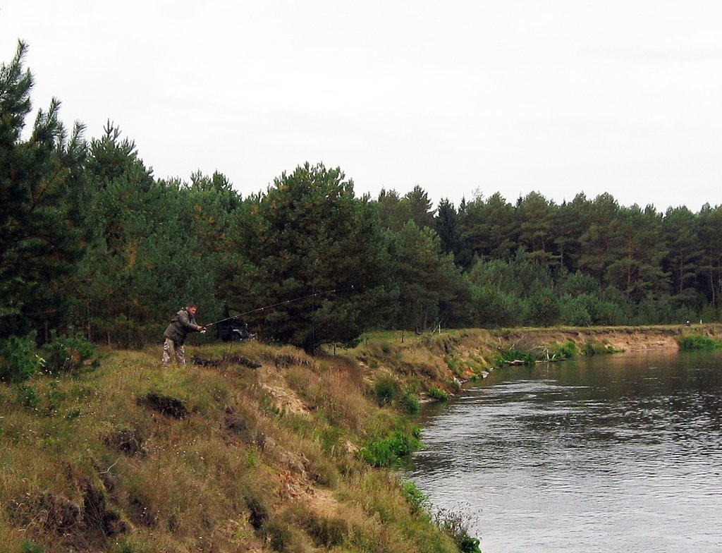 Рыболов с фидером на обрывистом берегу реки