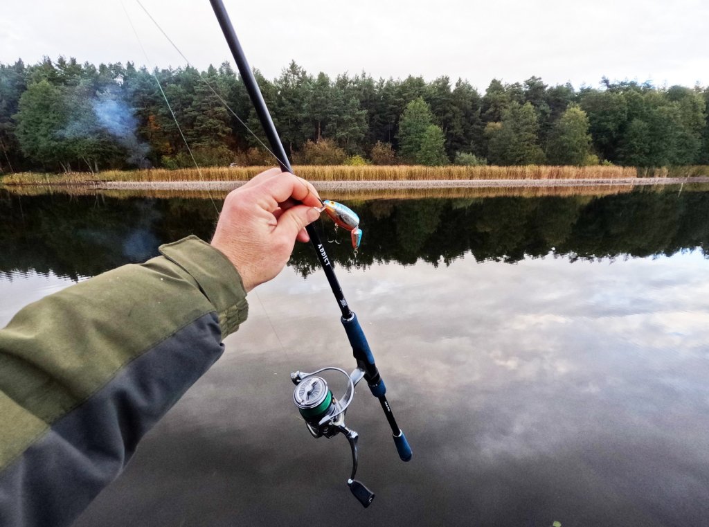 Спиннинг и приманка на фоне леса и водоёма