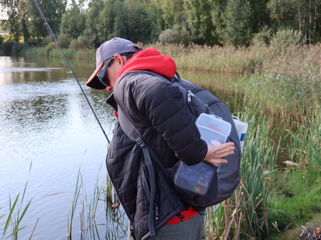 Спиннингист кладёт коробку в рюкзак