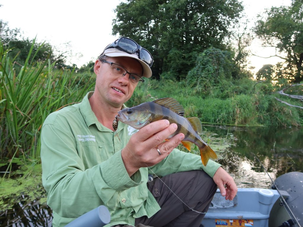 Валерий Сикиржицкий в лодке на реке держит окуня