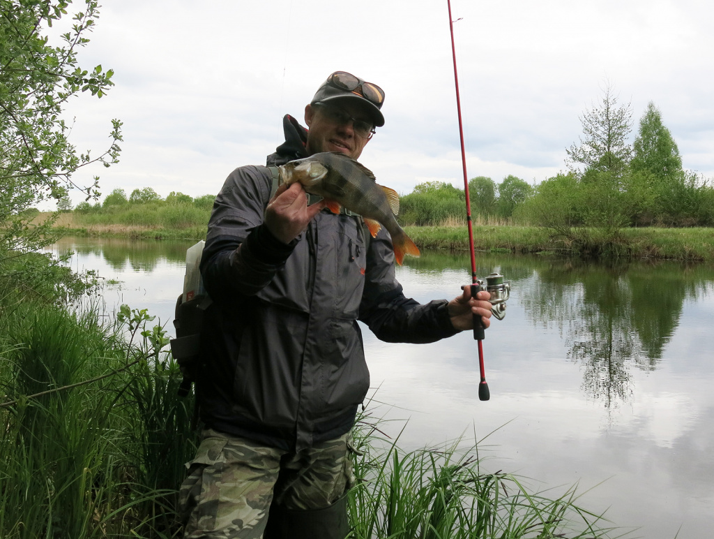 Спиннингист с пойманныйм окунем на фоне реки