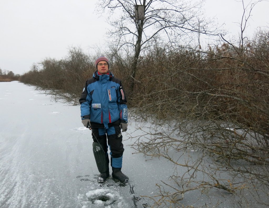Рыболов ловит со льда у берега водоёма