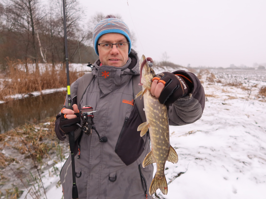 Рыбак с пойманной зимой на спиннинг щукой на берегу реки
