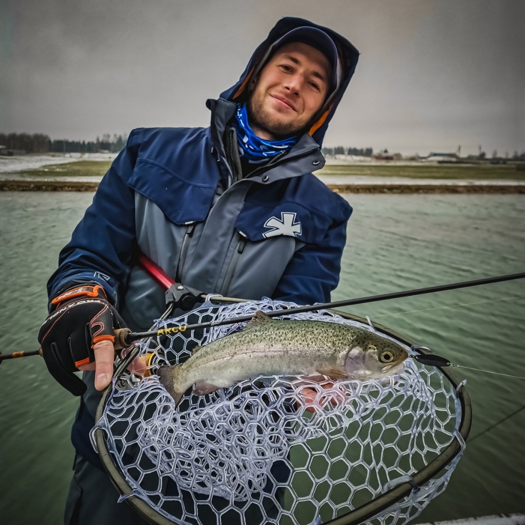 Рыболов держит пойманную форель в подсачеке