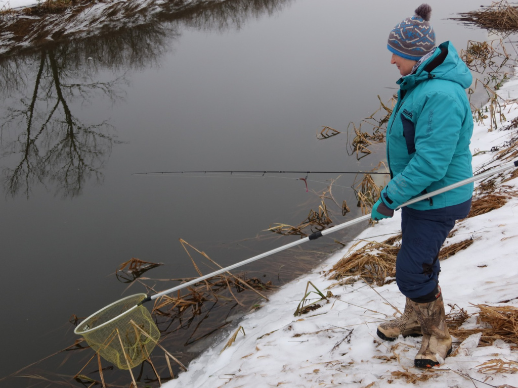 Рыбачка со спиннингом и подсаком на берегу реки зимой