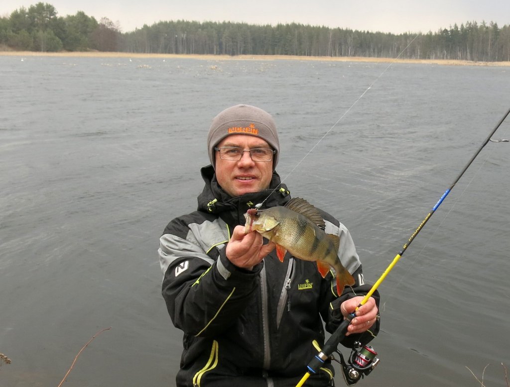 Валерий Сикиржицкий с окунем на фоне водоёма весной