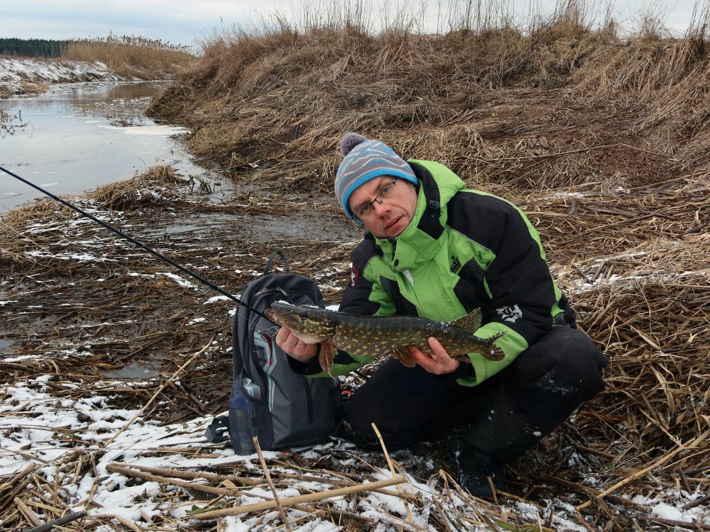 Рыболов со щукой на реке зимой