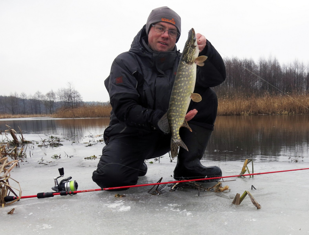 Рыбак с пойманной на спиннинг зимой щукой на реке