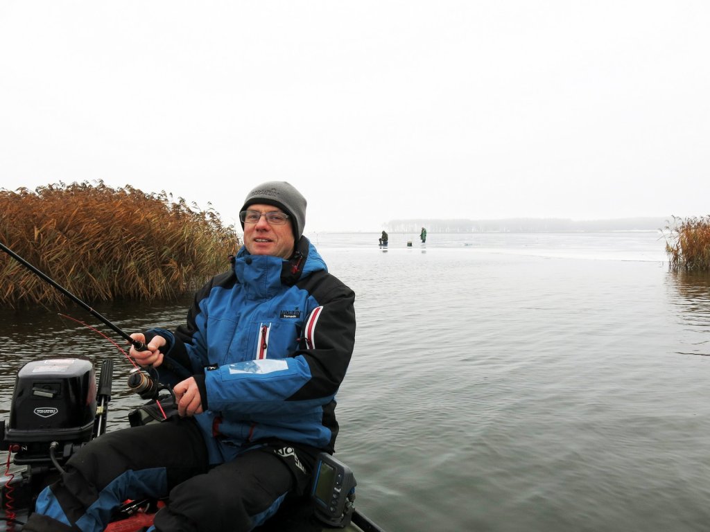 Спиннингист ловит в лодке зимой