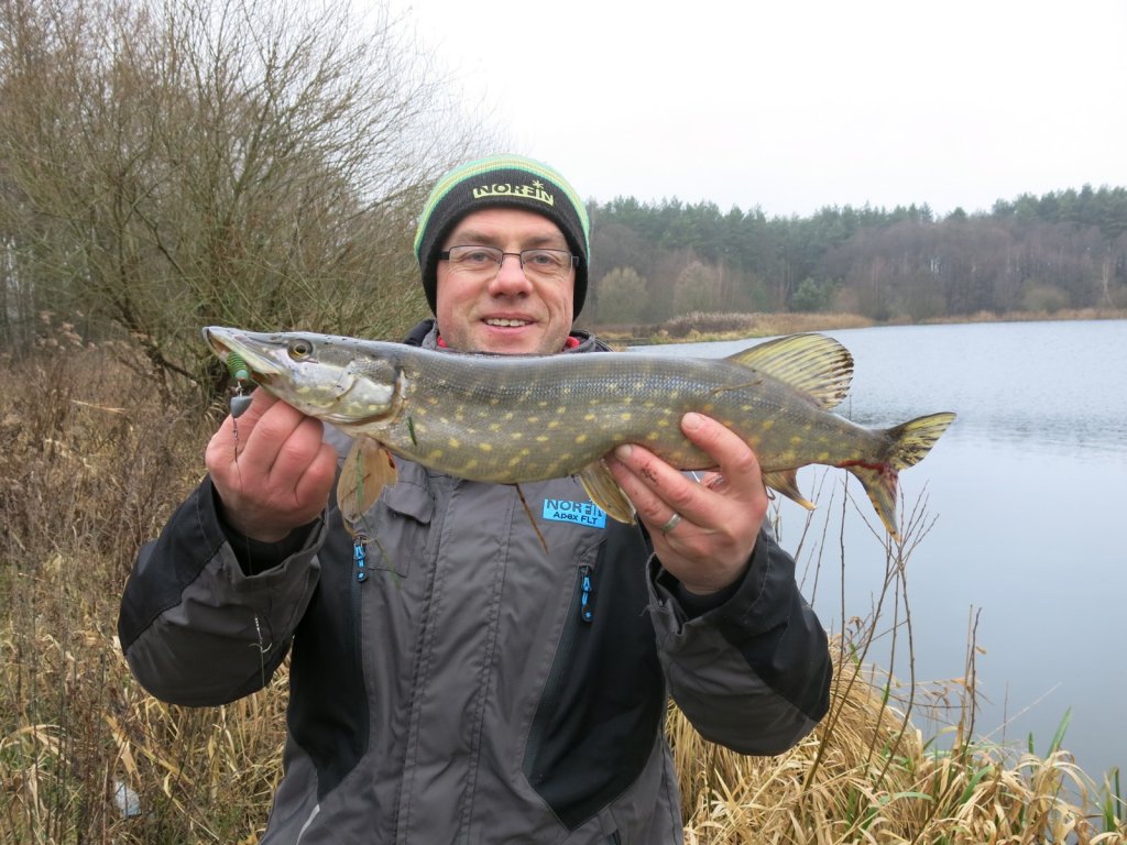 Валерий Сикиржицкий позирует со щукой на фоне водоёма