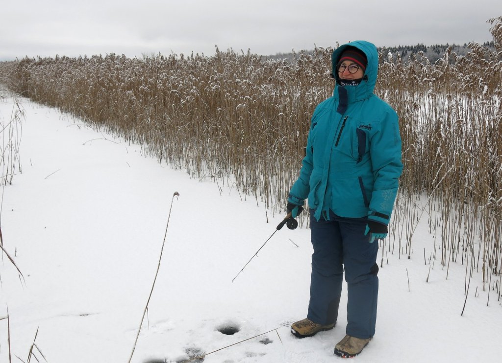 Рыбачка ловит со льда у тростника