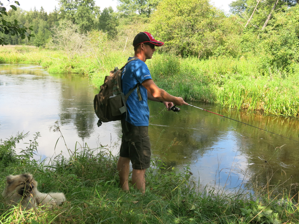 Спиннингист ловит рыбу на берегу реки вместе со своей собакой